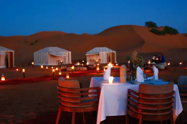 Mesa para dos alumbrada con farolillos sobre las dunas de Merzouga al caer la noche